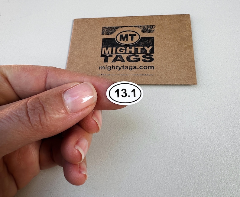 May include: White oval sticker with black text "13.1" on a white background. The sticker is being held by a hand.
