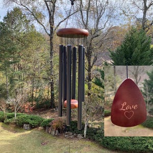 May include: A wind chime featuring a dark wooden top platform and six matte black metal tubes of varying lengths. A central wooden striker hangs among the tubes, and a triangular wooden wind catcher at the bottom is engraved with the word Love and a heart.