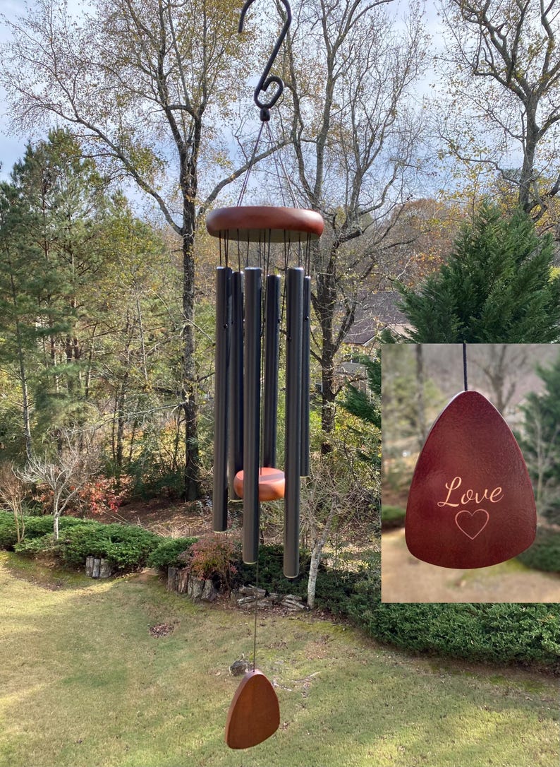 May include: A wind chime featuring a dark wooden top platform and six matte black metal tubes of varying lengths. A central wooden striker hangs among the tubes, and a triangular wooden wind catcher at the bottom is engraved with the word Love and a heart.