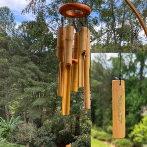 Op de afbeelding: Bamboe windgong met een natuurlijke afwerking. De windgong heeft een houten ring aan de bovenkant en verschillende bamboe buizen die eronder hangen. De buizen zijn verschillend van lengte en hebben uitgesneden secties.