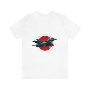 Peut inclure: T-shirt blanc avec un avion de chasse bleu volant au-dessus d'un cercle rouge, ressemblant au drapeau japonais.