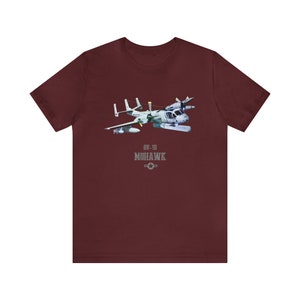 May include: A maroon t-shirt with a white and gray image of an OV-1D Mohawk aircraft. The text "OV-1D MOHAWK" is printed below the aircraft.