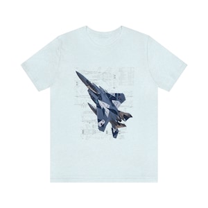 May include: A light blue t-shirt with a graphic of a fighter jet in camouflage colors. The jet is flying over a blueprint of the aircraft.