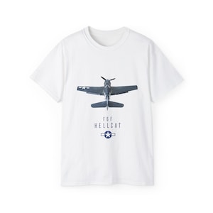 May include: White t-shirt featuring a detailed illustration of an F6F Hellcat airplane in navy blue. The text "F6F HELLCAT" is printed below the plane, along with a navy blue star emblem. The shirt is a classic crew neck style.