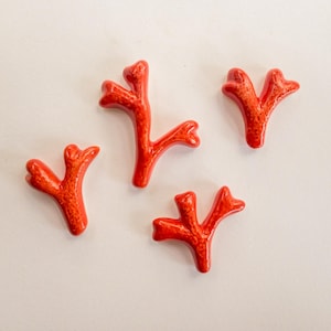 Puede incluir: Cuatro piezas individuales con forma de coral en color naranja brillante. Cada pieza presenta un acabado liso y brillante con detalles de superficie texturizados y porosos. Los objetos est&aacute;n dispuestos de forma dispersa, mostrando sus estructuras org&aacute;nicas &uacute;nicas de ramificaci&oacute;n en forma de Y.