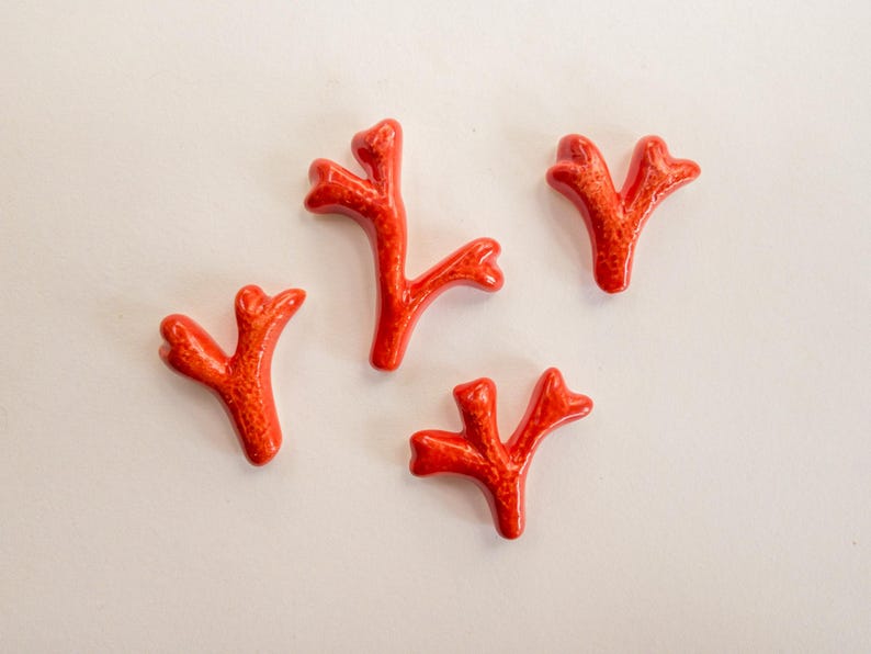 Puede incluir: Cuatro piezas individuales con forma de coral en color naranja brillante. Cada pieza presenta un acabado liso y brillante con detalles de superficie texturizados y porosos. Los objetos est&aacute;n dispuestos de forma dispersa, mostrando sus estructuras org&aacute;nicas &uacute;nicas de ramificaci&oacute;n en forma de Y.