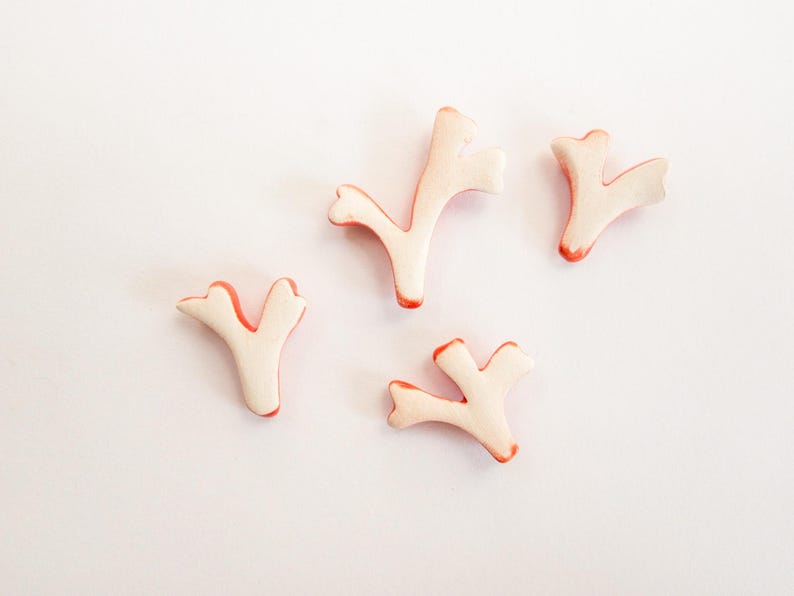 Puede incluir: Cuatro peque&ntilde;os adornos con forma de coral ramificado en color crema p&aacute;lido con bordes de color naranja rojizo vibrante. Cada pieza presenta una estructura en forma de Y con m&uacute;ltiples puntas, un acabado mate liso y formas org&aacute;nicas.
