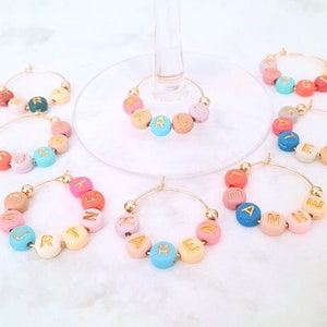 May include: Set of 8 gold-toned wine glass charms with colorful beads spelling out names. The names are: Courtney, Karen, Anne, Lexi, Layla, Karl, Susan, and Ginger.