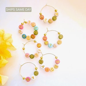 May include: Five gold hoop earrings with colorful beads spelling out different names. The names are: Celia, Harlow, Jaylen, Joyce, and Ava.