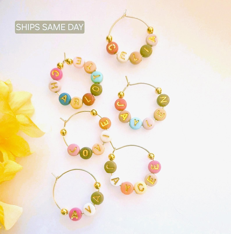 May include: Five gold hoop earrings with colorful beads spelling out different names. The names are: Celia, Harlow, Jaylen, Joyce, and Ava.