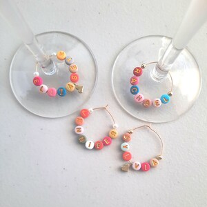 May include: Four colorful glass charms with gold letters spelling out the names "Elizabeth", "Rachel", "Jennifer", and "Sylvia". Each charm has a small gold heart attached.