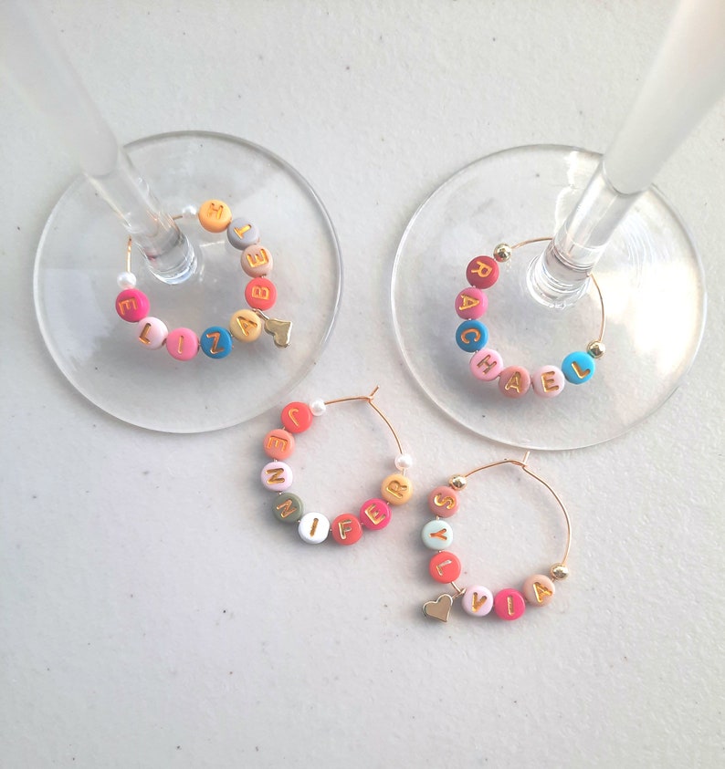May include: Four colorful glass charms with gold letters spelling out the names "Elizabeth", "Rachel", "Jennifer", and "Sylvia". Each charm has a small gold heart attached.
