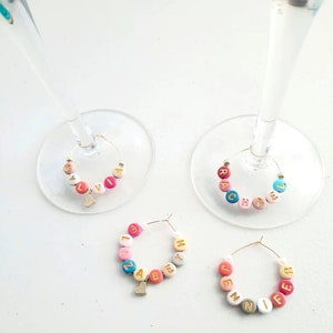 May include: Four colorful glass charms with gold letters spelling out the names "Sylvia", "Rachel", "Elizabeth", and "Jennifer". Each charm has a small gold heart hanging from it.
