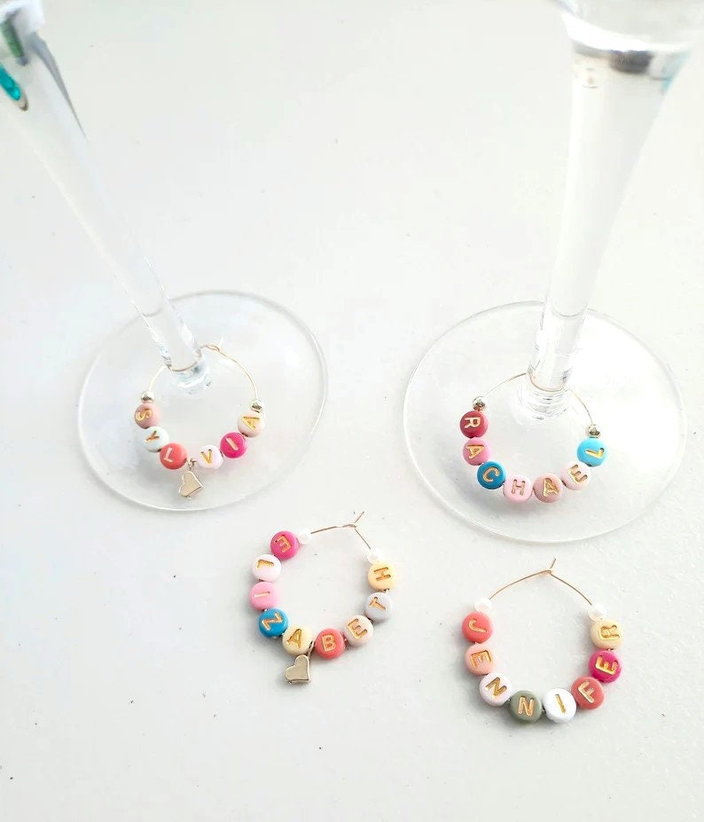 May include: Four colorful glass charms with gold letters spelling out the names "Sylvia", "Rachel", "Elizabeth", and "Jennifer". Each charm has a small gold heart hanging from it.