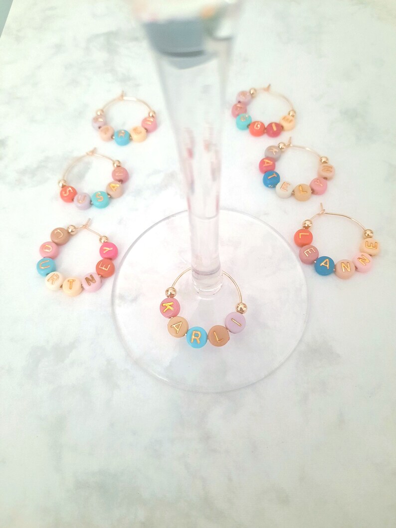 May include: Set of six colorful glass charms with gold wire hoops. Each charm has a different name spelled out in gold letters on colorful beads. The names are:  Suzy,  Katie,  Kelly,  Ellie,  Anne, and  Karli.
