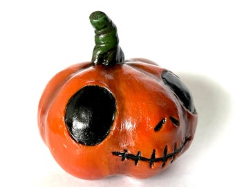 以下が含まれることがあります： ハロウィーンの装飾に最適な、彫刻された顔を持つ小さなオレンジ色のカボチャの置物。カボチャは、大きな黒い眼窩、縫い付けられた口、緑色の茎が特徴です。光沢のある仕上がりは、洗練された外観を与えます。