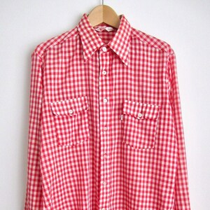 Peut inclure: Une chemise à manches longues à carreaux vichy rouge et blanc avec deux poches à rabat.