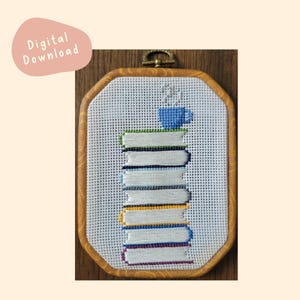 May include: Cross-stitch embroidery in a wooden hoop featuring a stack of books with a blue coffee cup on top. The books have different colored spines. The words "Digital Download" are in a pink oval in the upper left corner.