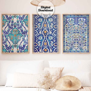 Op de afbeelding: Drie ingelijste prints van blauwe en witte gepatroneerde tegels met bloemmotieven. De tegels zijn in een rij op een witte muur gerangschikt. De prints bevinden zich in een woonkamer met een witte bank, een salontafel en een vaas met gedroogde bloemen.