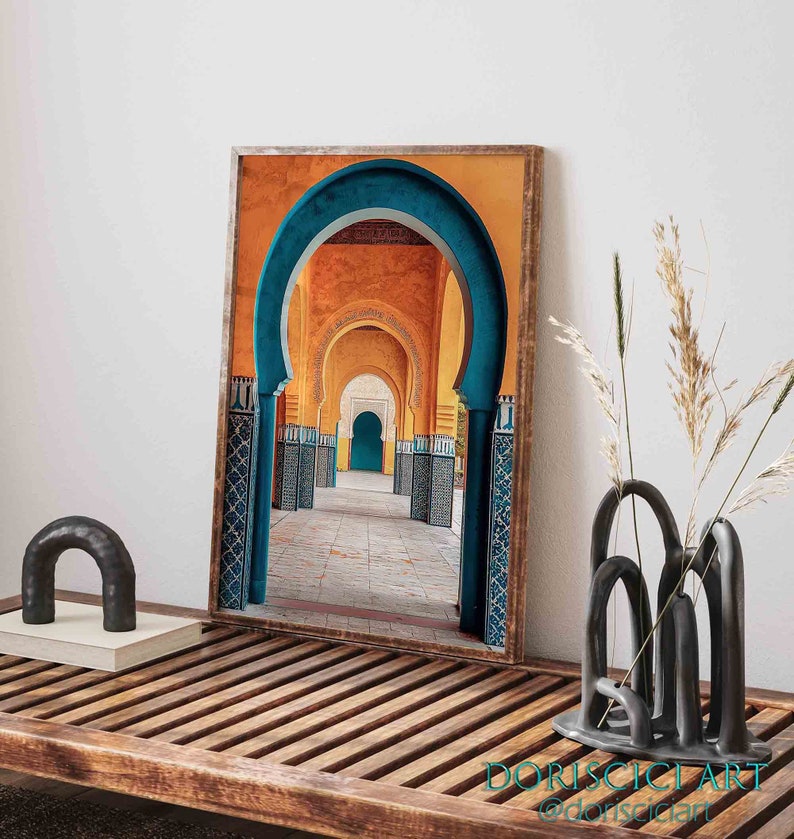 May include: A framed photograph of a colorful archway in a Moroccan building. The archway is made of blue and yellow tiles and leads to a courtyard with a blue door.