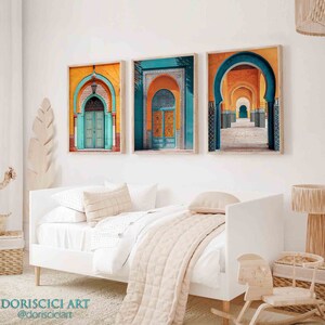 May include: Three framed prints of colorful Moroccan architecture with arched doorways and intricate tilework. The prints are hung on a white wall above a white daybed with a beige throw blanket.