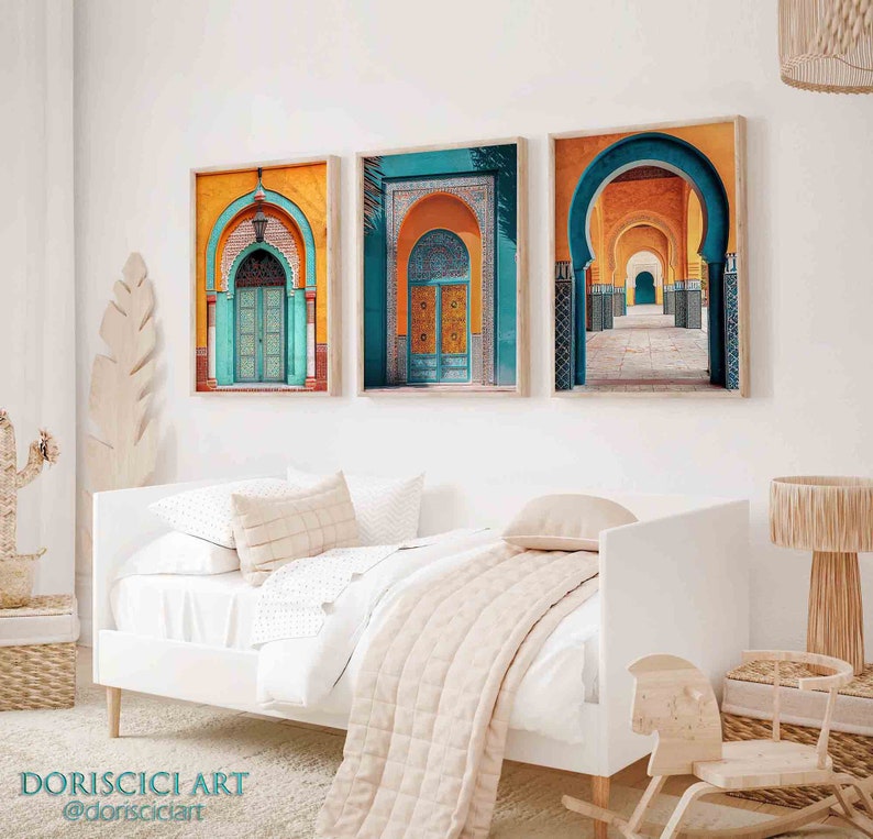 May include: Three framed prints of colorful Moroccan architecture with arched doorways and intricate tilework. The prints are hung on a white wall above a white daybed with a beige throw blanket.