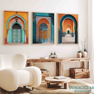 May include: Three framed prints of colorful archways in a Moroccan style. The prints are hung on a white wall above a wooden table with a white armchair and a wooden coffee table.