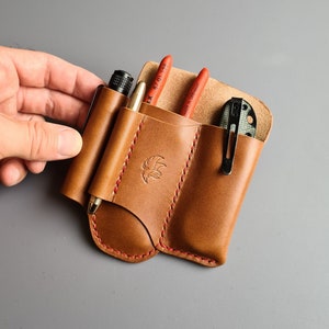 May include: A brown leather multi-tool carrying case with red stitching. The case has three slots for tools and a fourth slot for a small knife. The case is empty.