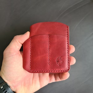 May include: A red leather wallet with three slots and a stitched design. The wallet has a small logo on the front.