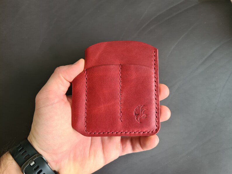 May include: A red leather wallet with three slots and a stitched design. The wallet has a small logo on the front.