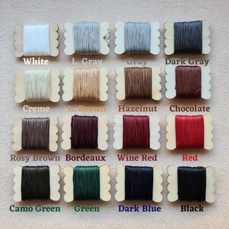 May include: A collection of 14 spools of waxed thread in various colors, including white, gray, brown, red, green, and blue. Each spool is labeled with its color name.