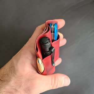 May include: A red leather carrying case with a black flashlight, a gold pen, and a blue multi-tool inside.