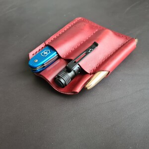 May include: A burgundy leather pocket organizer with three slots. A blue pocket knife, a black flashlight, and a gold pen are in the slots.