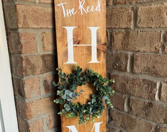 May include: A wooden sign with the words "The Reed Home Est. 1981" in white paint. The letter "O" in the word "Home" is replaced with a small green wreath.