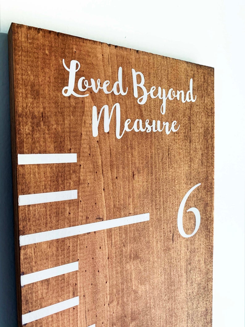 May include: A brown wooden growth chart with white markings and the text "Loved Beyond Measure" and the number "6" at the top.