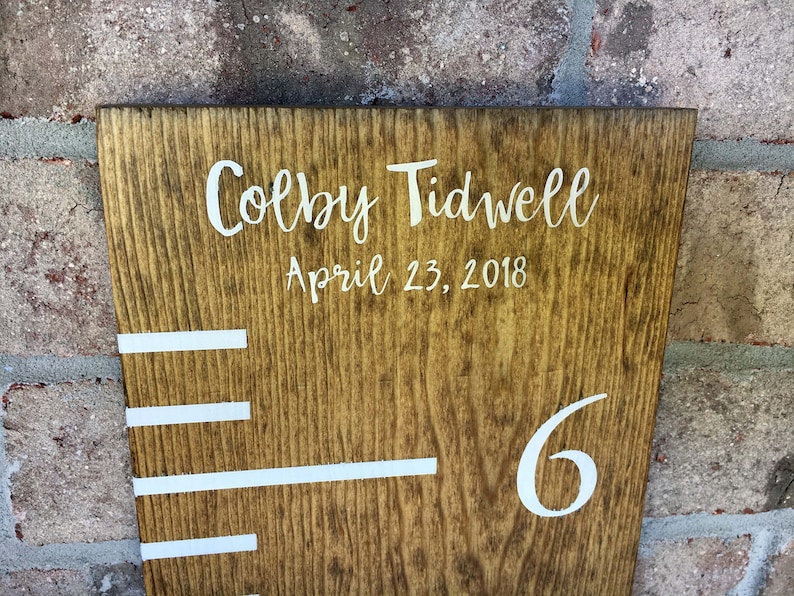 May include: A wooden growth chart with white markings and the name "Colby Tidwell" and the date "April 23, 2018" written on it. The number "6" is also visible on the chart.