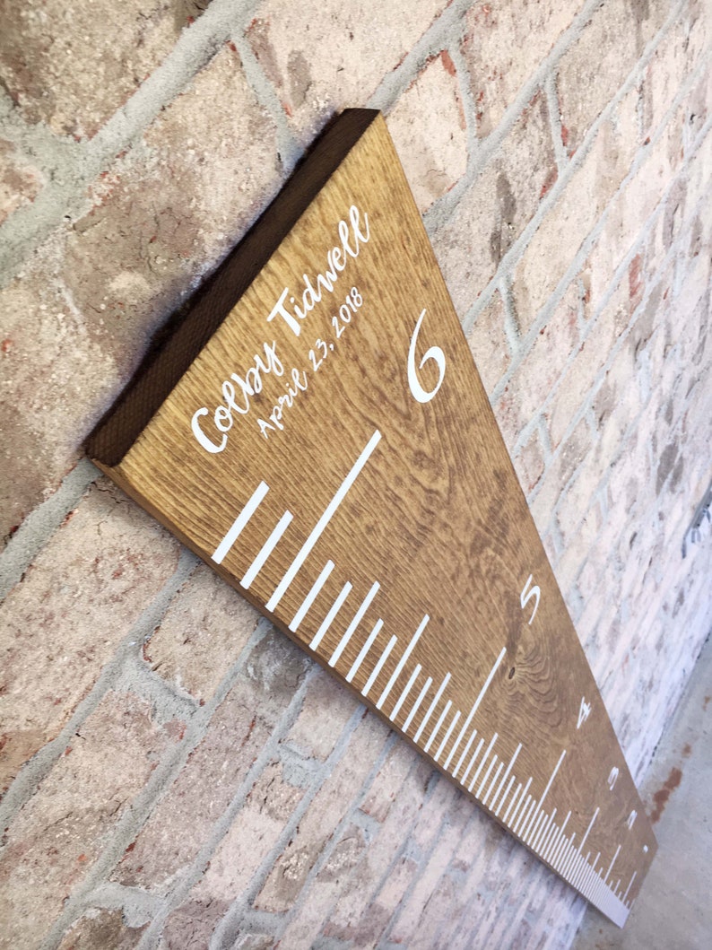 May include: A wooden growth chart with white markings and numbers. The chart is personalized with the name "Colby Tidwell" and the date "April 23, 2018".