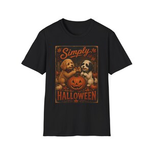 May include: A black short-sleeved t-shirt featuring a graphic print of two dogs sitting behind a carved jack-o'-lantern pumpkin. The design includes autumn leaves, smaller pumpkins, and the text Simply HALLOWEEN in orange lettering.