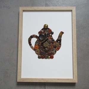 Puede incluir: Una obra de arte enmarcada que representa una tetera hecha de varios botones en tonos marrones, naranjas y dorados.