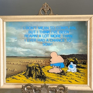May include: Framed artwork with a cartoon figure in blue shorts and a small white dog in a field of hay bales. The text reads, "I DON'T MEAN TO COMPLAIN, ...BUT I THINK I'VE BEEN REAPIN' A LOT MORE THAN I EVER HAD A CHANCE TO SOW!"