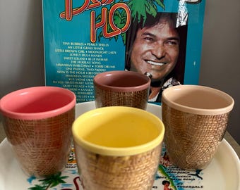May include: Four brown and beige ceramic mugs with a woven pattern, sitting on a white tray with a map of Florida and a pink flamingo. The tray is next to a vintage record album with a blue background and the text "Hawaiian 30 Favorites Don Ho" in red and white.