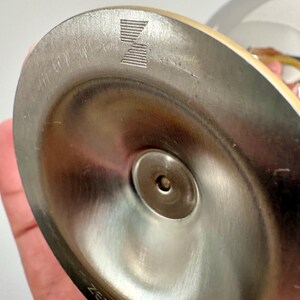 May include: Close-up of a stainless steel base of a Zepter product. The base is circular with a central indentation and a visible logo. The word "ZEPTER" is etched on the side of the base.