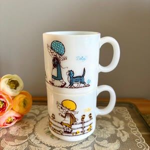 May include: A white ceramic mug with a black handle and the text "But First, Coffee" in a black, handwritten-style font. The mug is on a white surface.