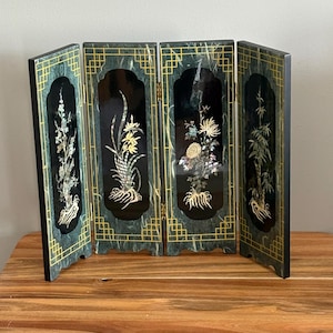 May include: A four-panel folding screen with a black background and floral designs. The screen has a green marble-like border with gold accents. The floral designs are made of mother-of-pearl.