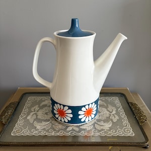 May include: White ceramic teapot with a blue lid and a band of orange and white daisy flowers around the bottom.
