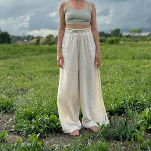 K&ouml;nnte beinhalten: Eine Person tr&auml;gt ein hellgr&uuml;nes Tanktop und eine wei&szlig;e, weite Hose und steht auf einem Feld mit gr&uuml;nem Gras. Der Himmel ist bew&ouml;lkt und blau.