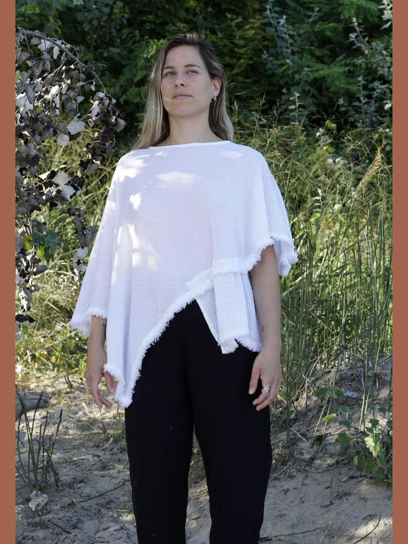 May include: A white, asymmetrical, lightweight poncho with a frayed edge. The poncho is made of a soft, breathable fabric and has a relaxed fit.