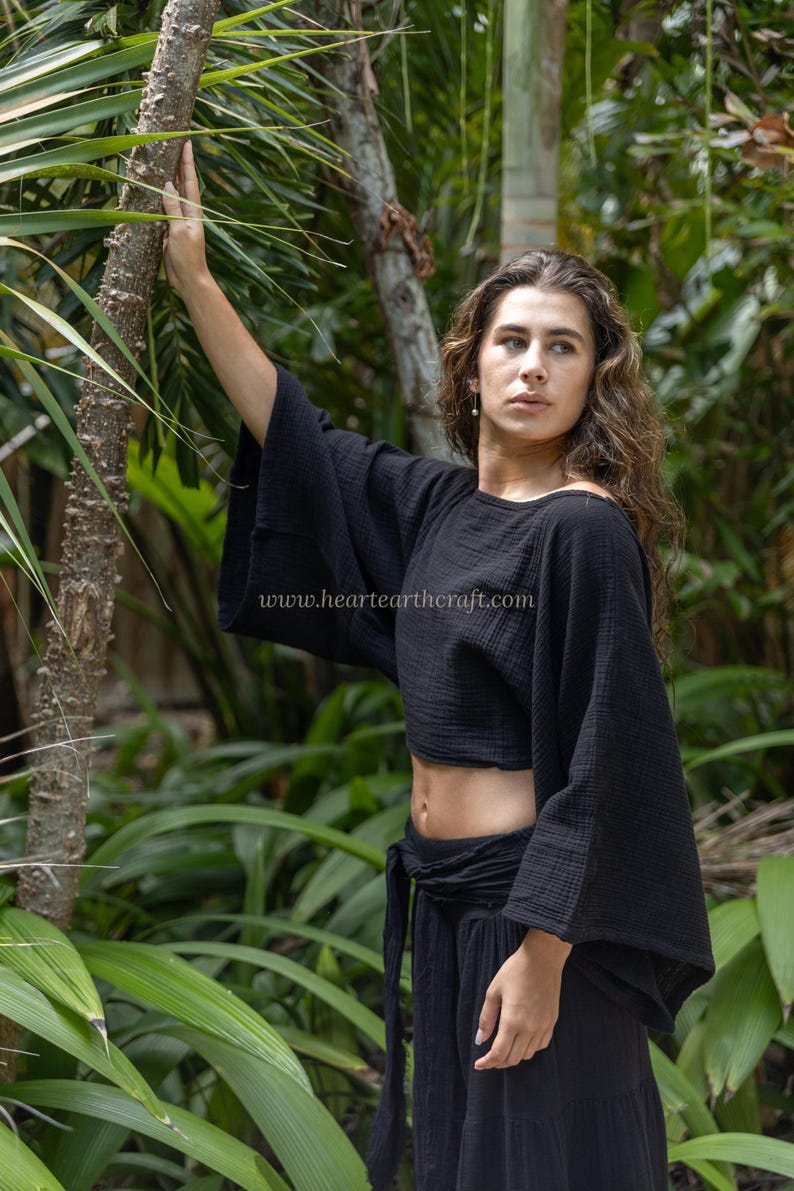 May include: A black cropped top with wide, loose-fitting sleeves and a textured fabric finish. The garment features a round neckline and a boxy silhouette. The text www.heartearthcraft.com is printed in white across the center of the black fabric.