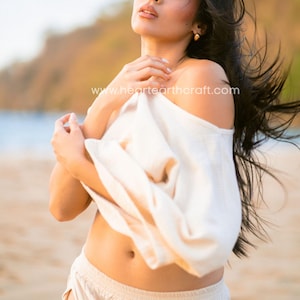 May include: A cream-colored off-the-shoulder top and matching cream-colored pants. The top features a loose, draped fit, while the pants have a high-waisted design. The text www.heartearthcraft.com is visible across the center of the image.