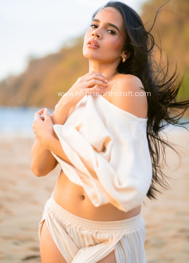 May include: A cream-colored off-the-shoulder top and matching cream-colored pants. The top features a loose, draped fit, while the pants have a high-waisted design. The text www.heartearthcraft.com is visible across the center of the image.